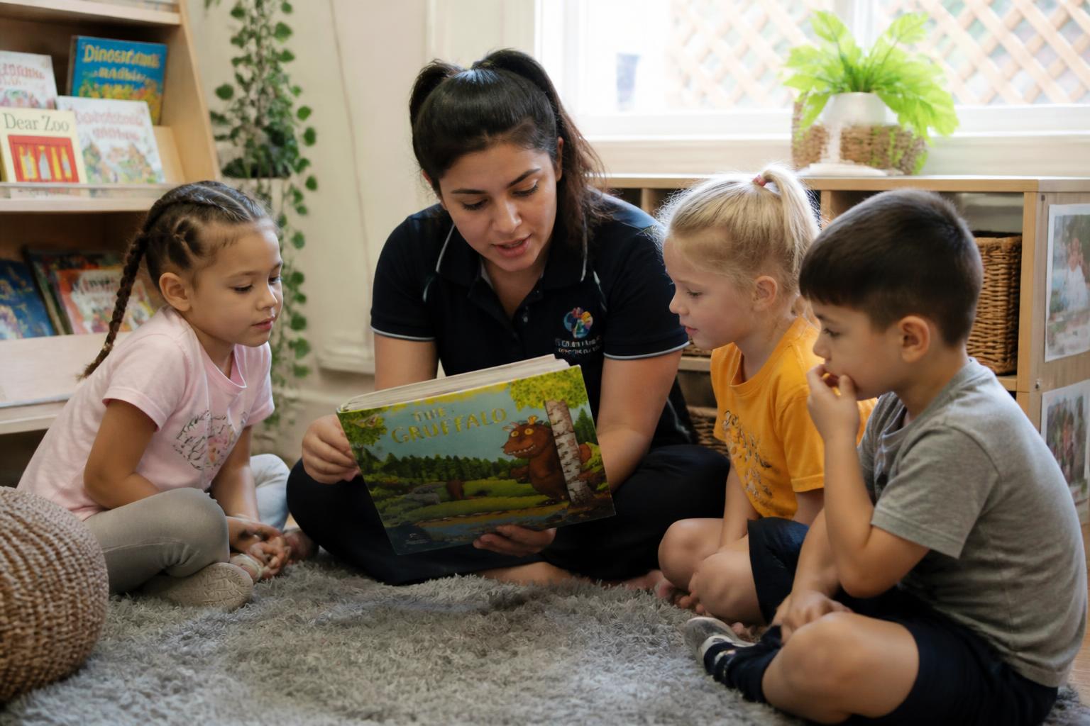 Pedagogisch medewerker leest voor aan drie kinderen in de leeshoek