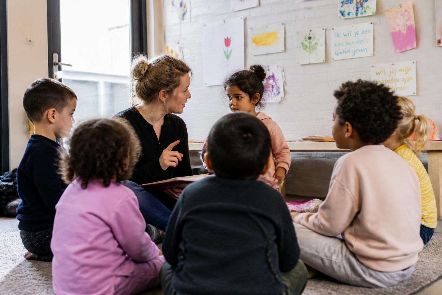 Kinderen zitten in een kring op de mat te luisteren naar een verhaal van de pedagogisch medewerker